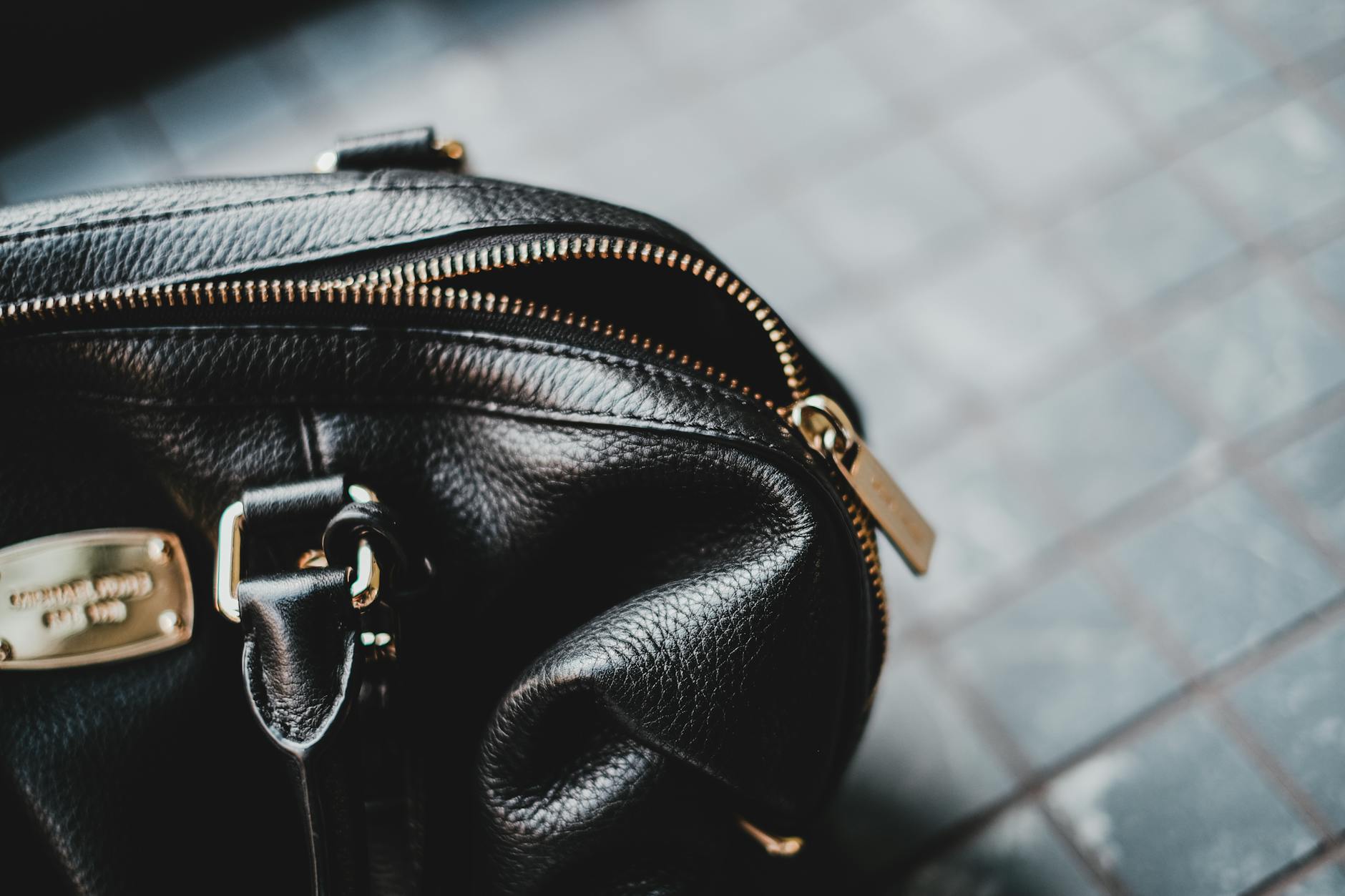 Close-up of a stylish black leather bag featuring a zipper and metal tag.